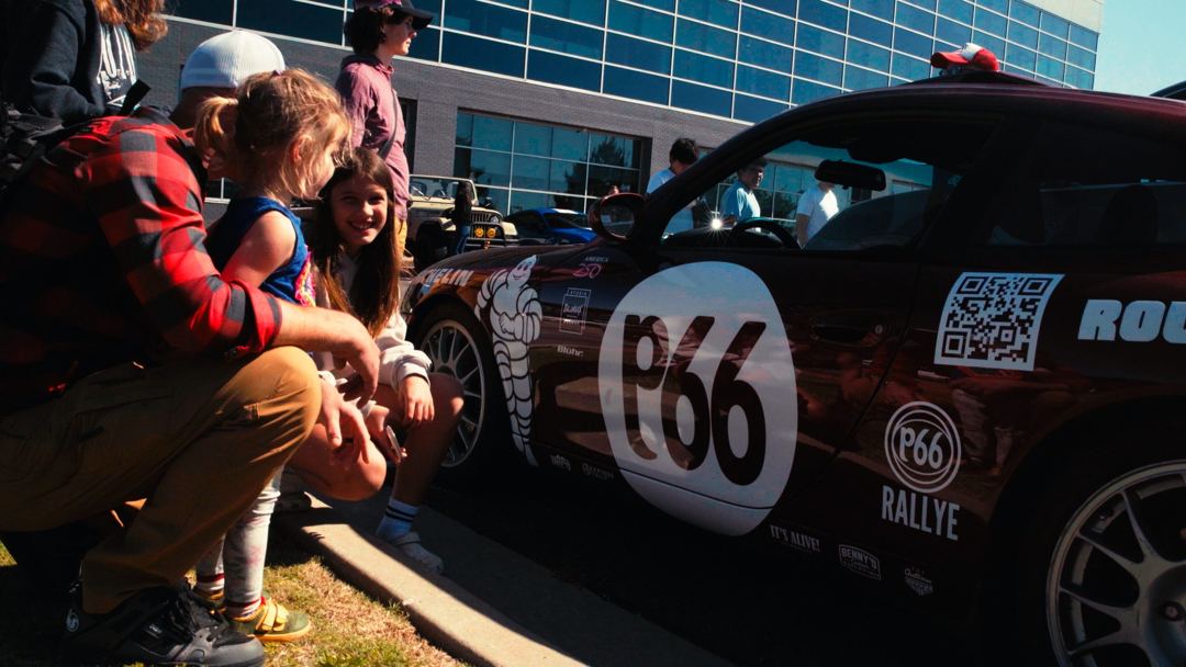 A family at the roadside looking over the P66 Rallye car at a public stop